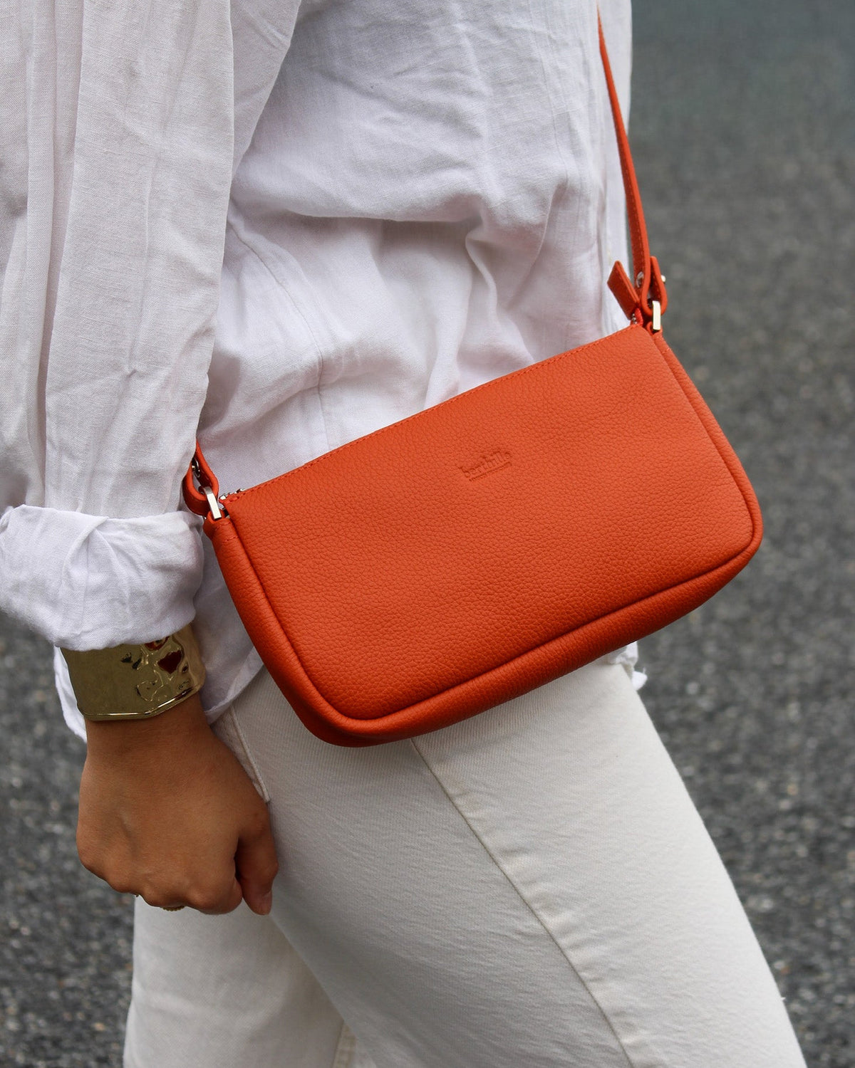 Femme portant la pochette Berthe en cuir vachette coloris orange terracotta en bandoulière – Berthille Maison Française