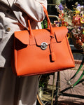 Femme portant sac Cortina cuir orange à la main en ville