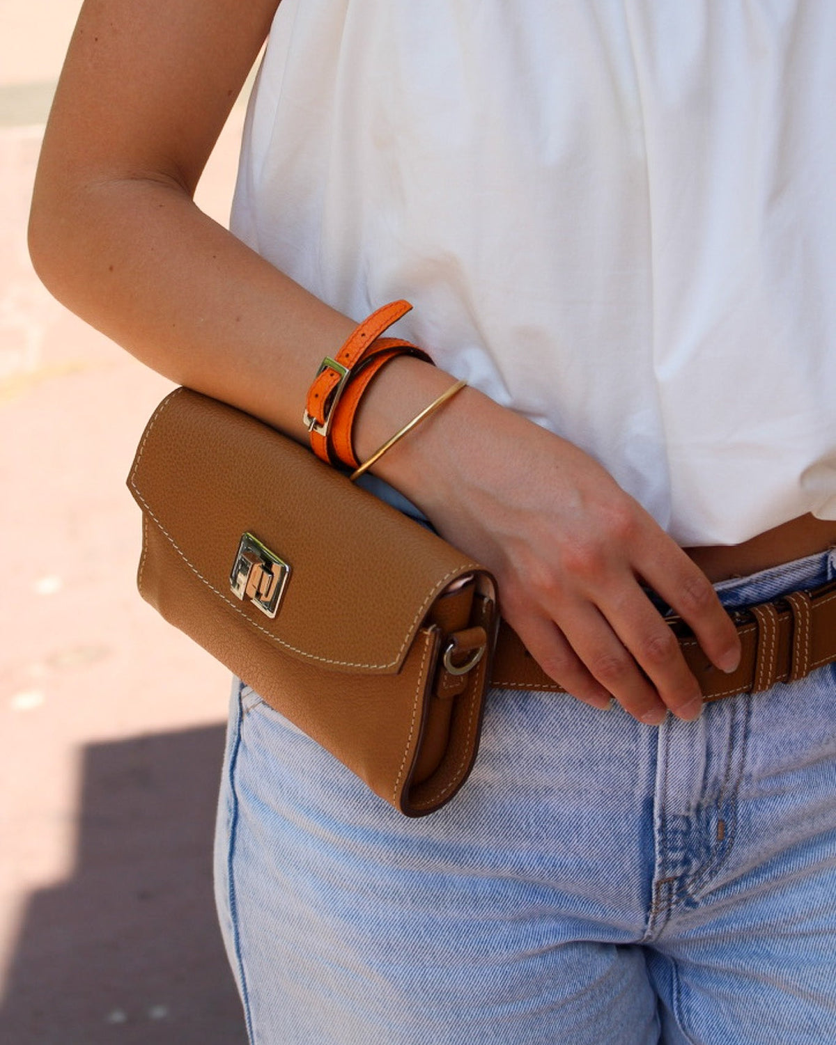 Pochette cuir en couleur caramel porter autour d'une ceinture par une femme avec un bracelet orange 