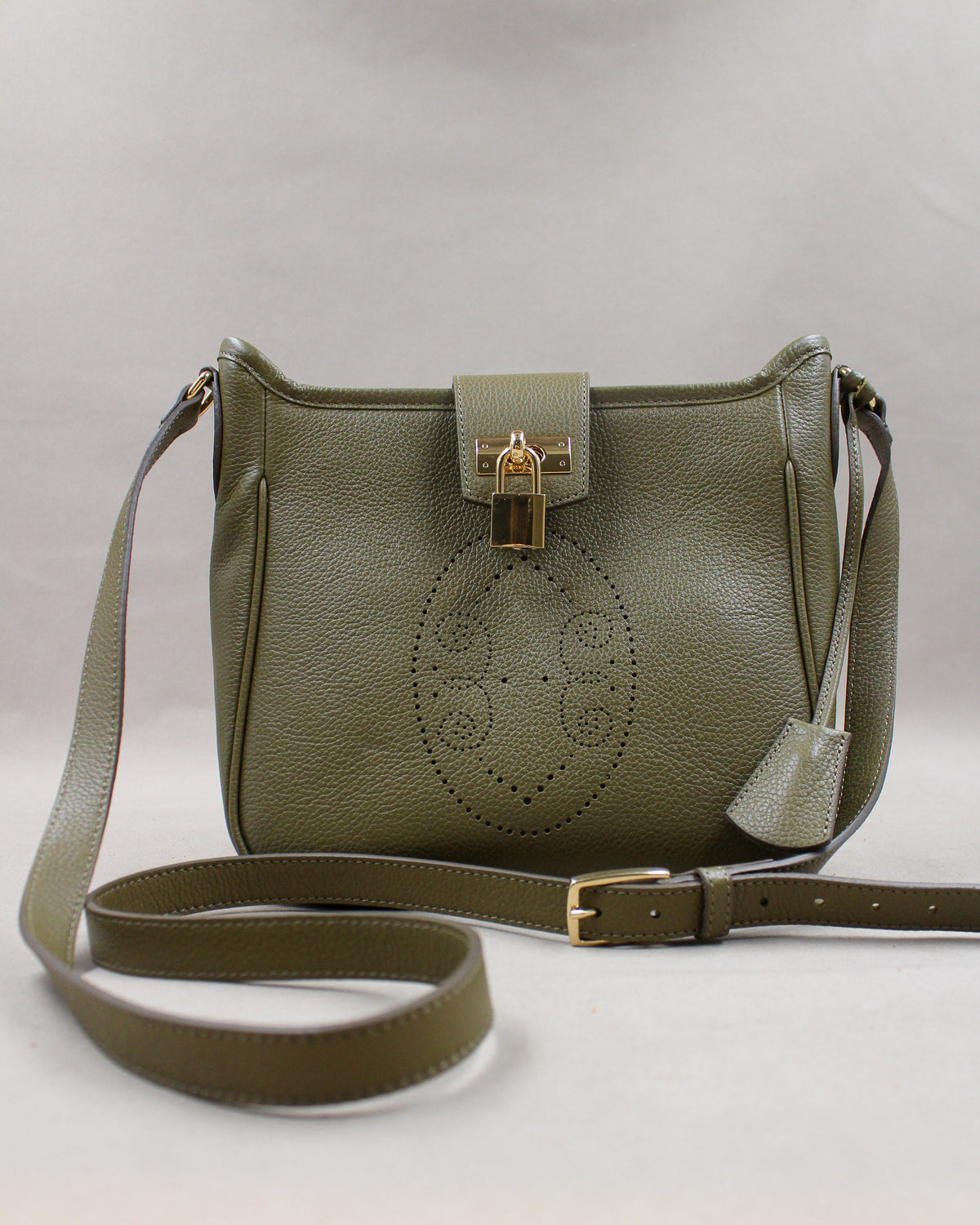Sac Trianon en cuir kaki vue de face, motif perforé bout fleuri, cadenas doré, clochette en cuir et bandoulière réglable, fabriqué en France par Berthille