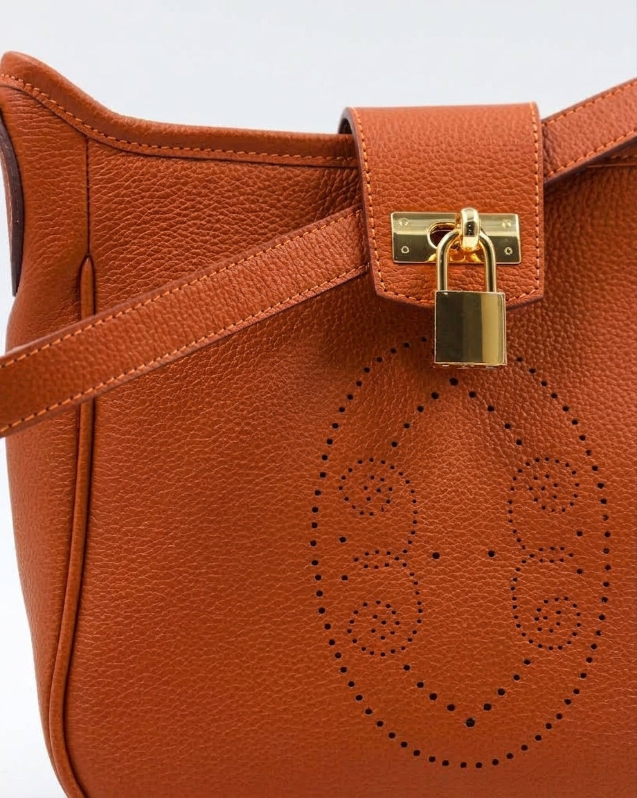 Gros plan sur le motif perforé bout fleuri du sac Trianon en cuir orange grainé, cadenas doré et coutures sellier, savoir-faire artisanal français